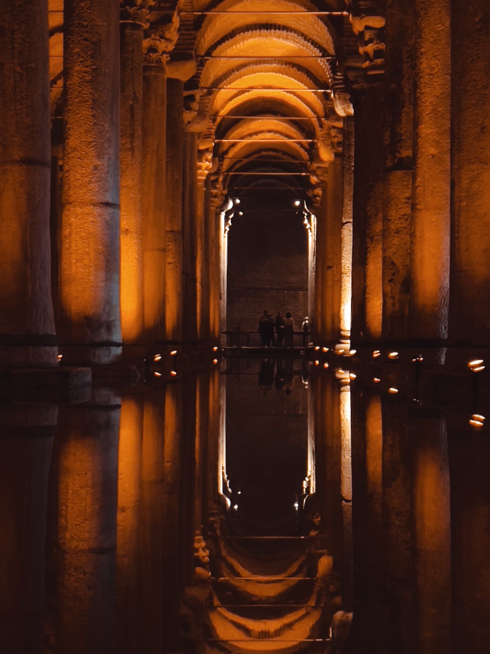 Beleuchtete Säulen und Ziegelgewölbe der Basilika-Zisterne spiegeln sich im stillen Wasser, Besucher auf dem Steg, Istanbul