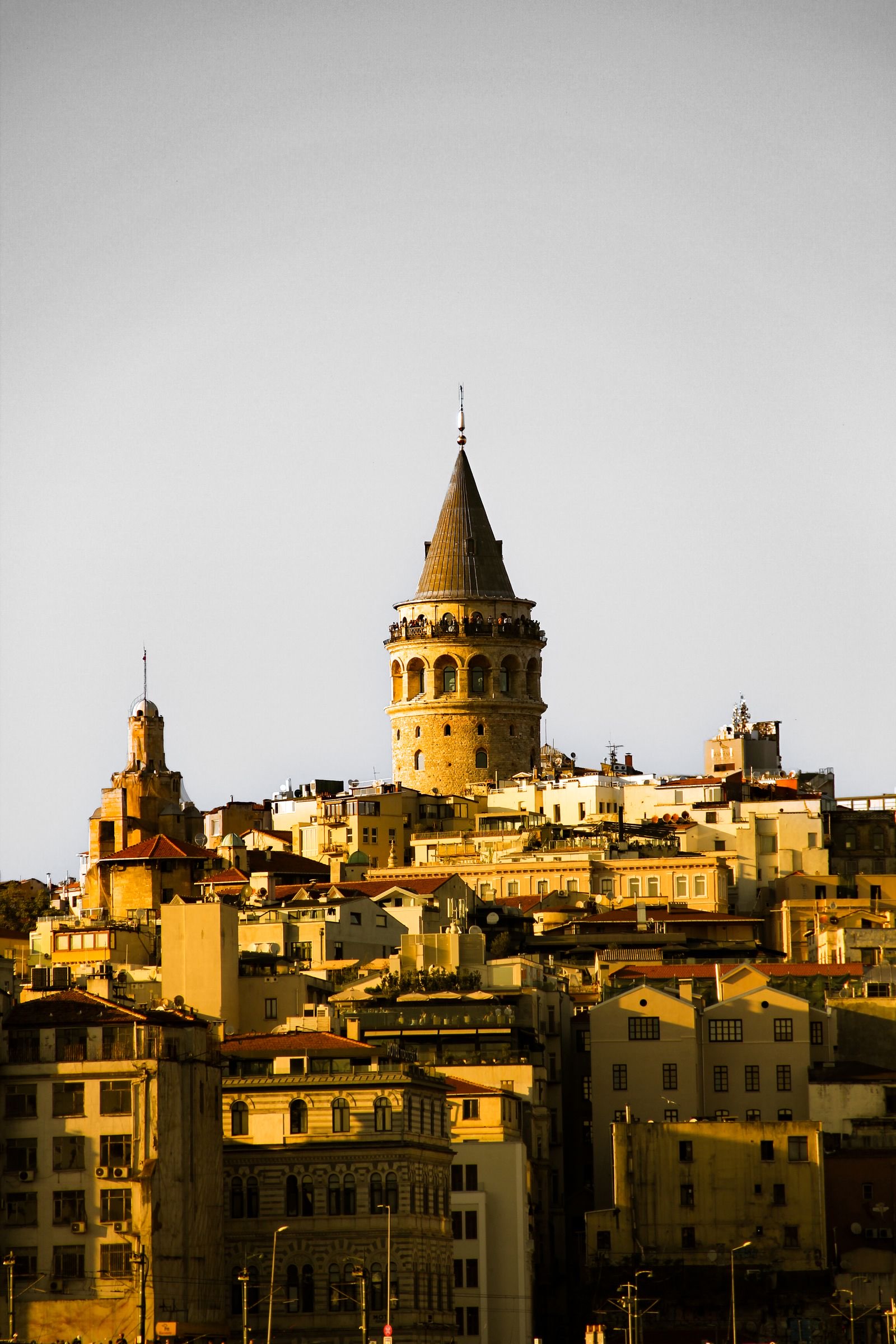 Der Galataturm mit kegelförmigem Dach und Aussichtsgalerie über den Dächern von Karaköy und Beyoğlu im warmen Abendlicht, Istanbul