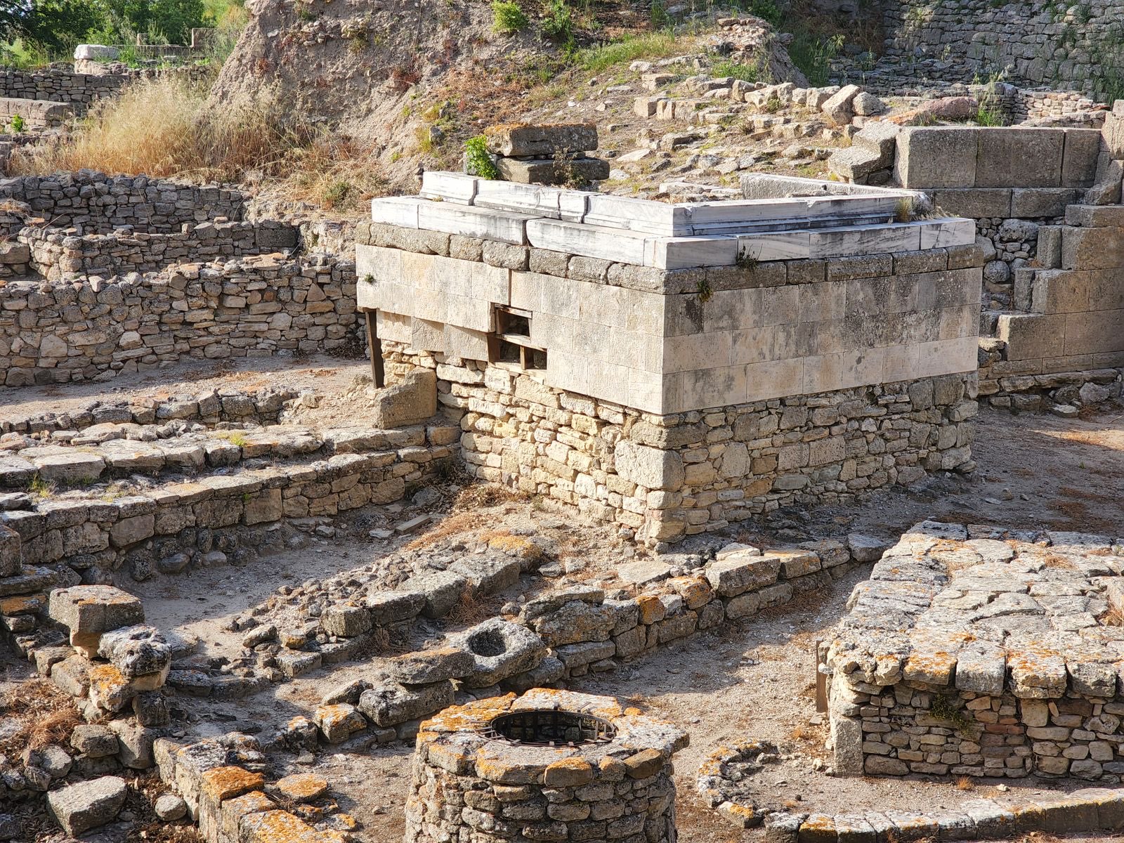 Steinmauern, ein marmorbedecktes Heiligtum und ein runder Brunnen zwischen den ausgegrabenen Ruinen von Troja bei Çanakkale
