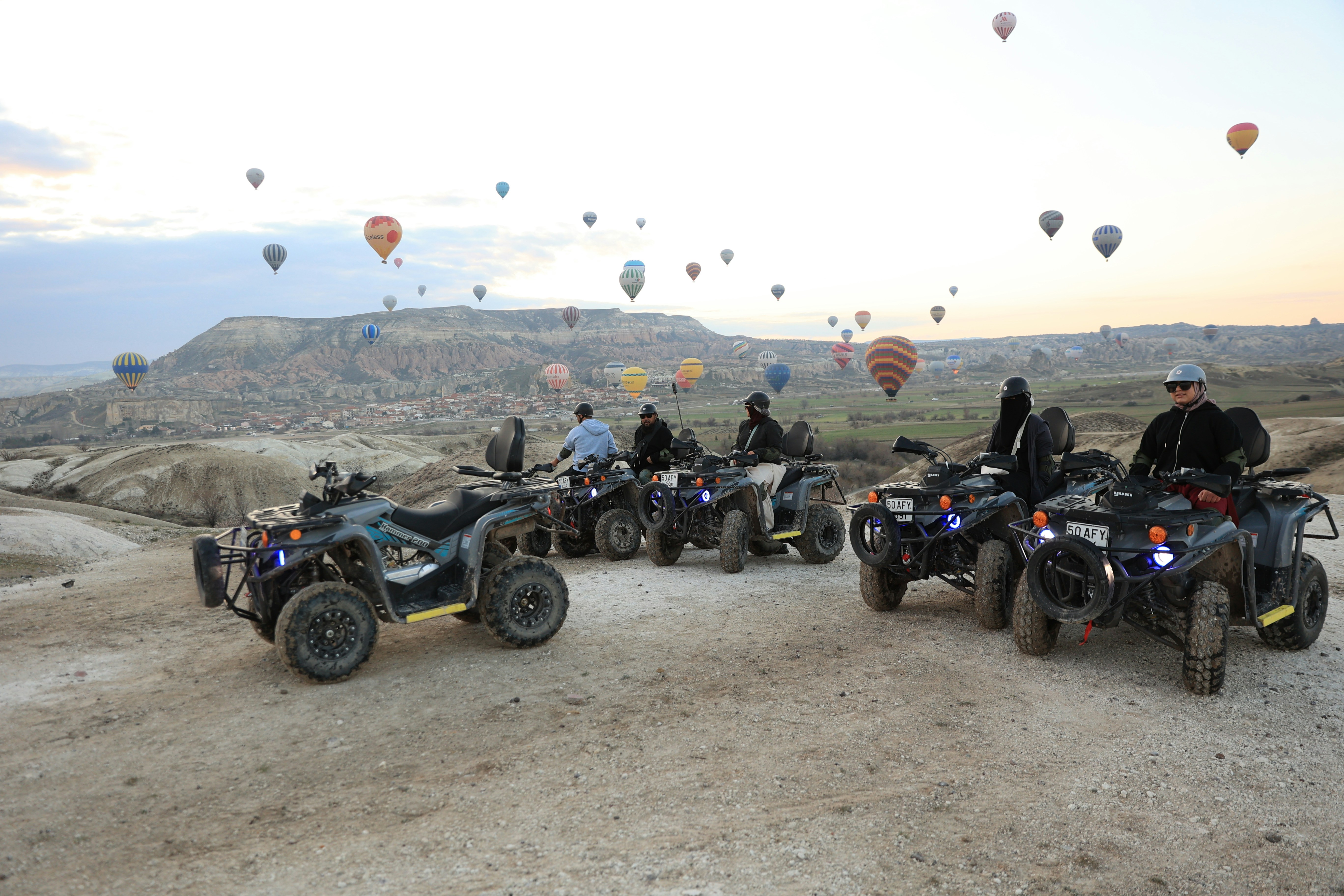 Group of riders on ATVs with dozens of hot air balloons above Cappadocia at sunrise, Turkey