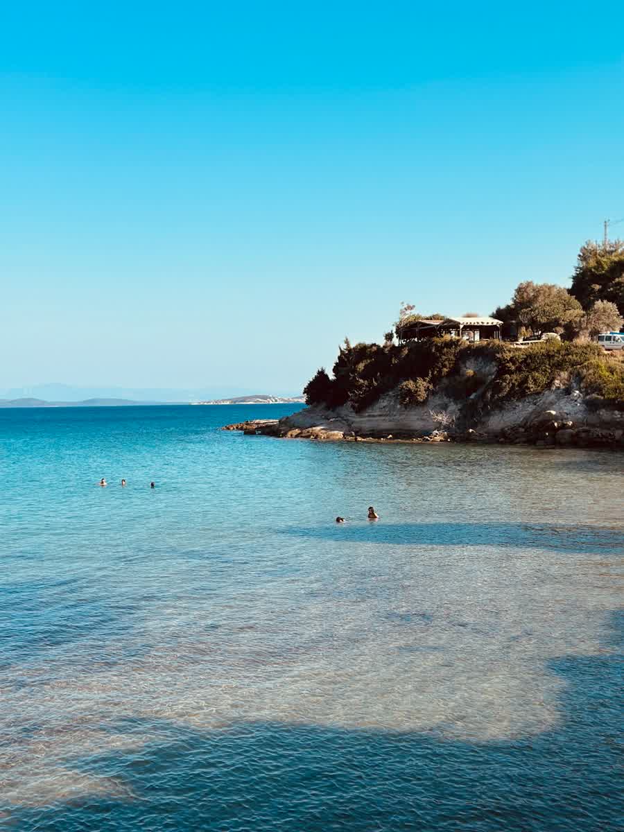 Clear turquoise water with people swimming near a rocky Aegean coast at Çeşme, Turkey