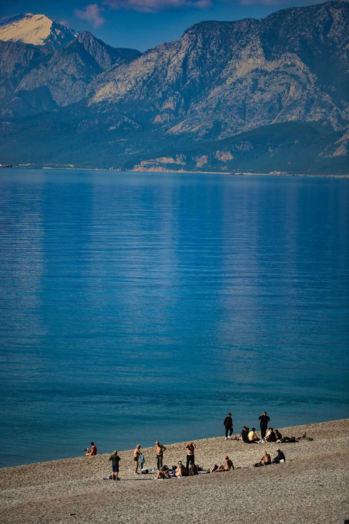 Tourists on a pebble beach with Taurus Mountains backdrop, Antalya coast, Turkey