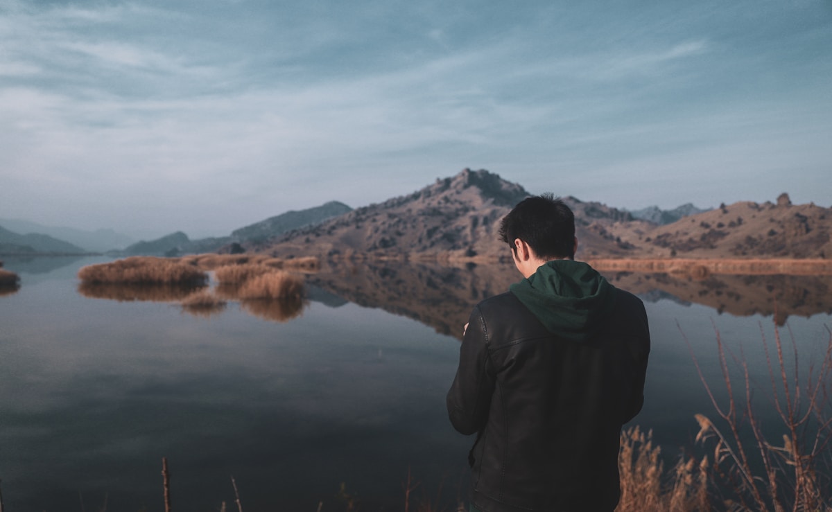 Man standing at the edge of a calm lake with rocky mountains reflected in the still water, eastern Turkey