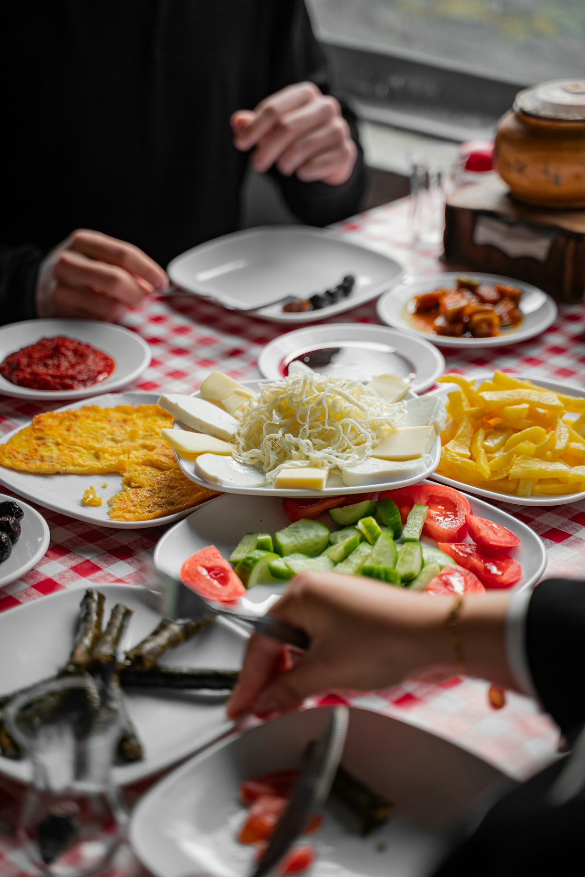 Traditional Turkish breakfast spread with cheese, eggs, olives, vegetables and omelette on red-checked tablecloth