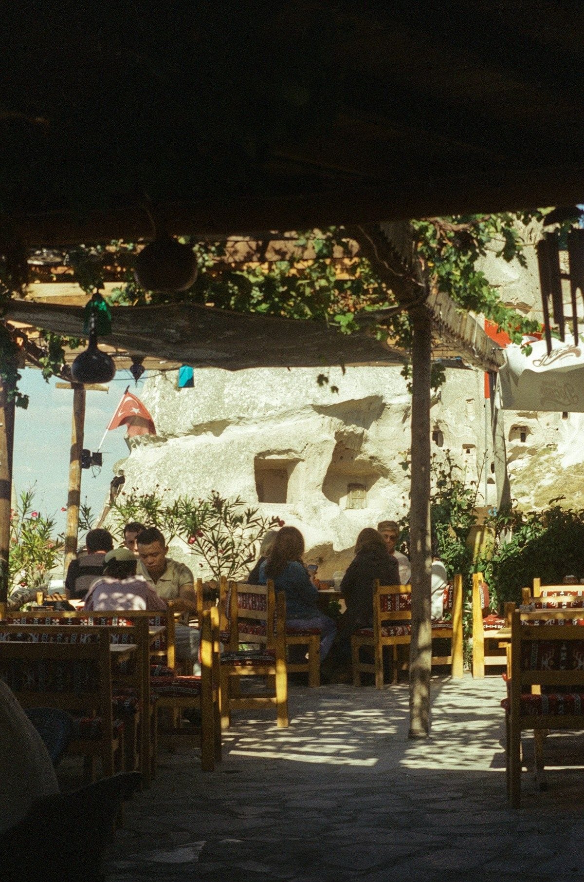 Outdoor terrace restaurant with diners seated in front of carved cave rock buildings in Cappadocia, Turkey