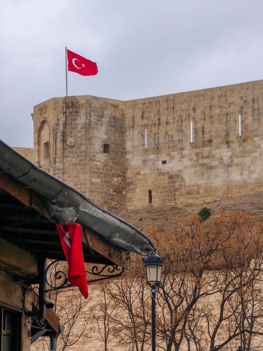 Gaziantep Castle with a Turkish flag under cloudy skies