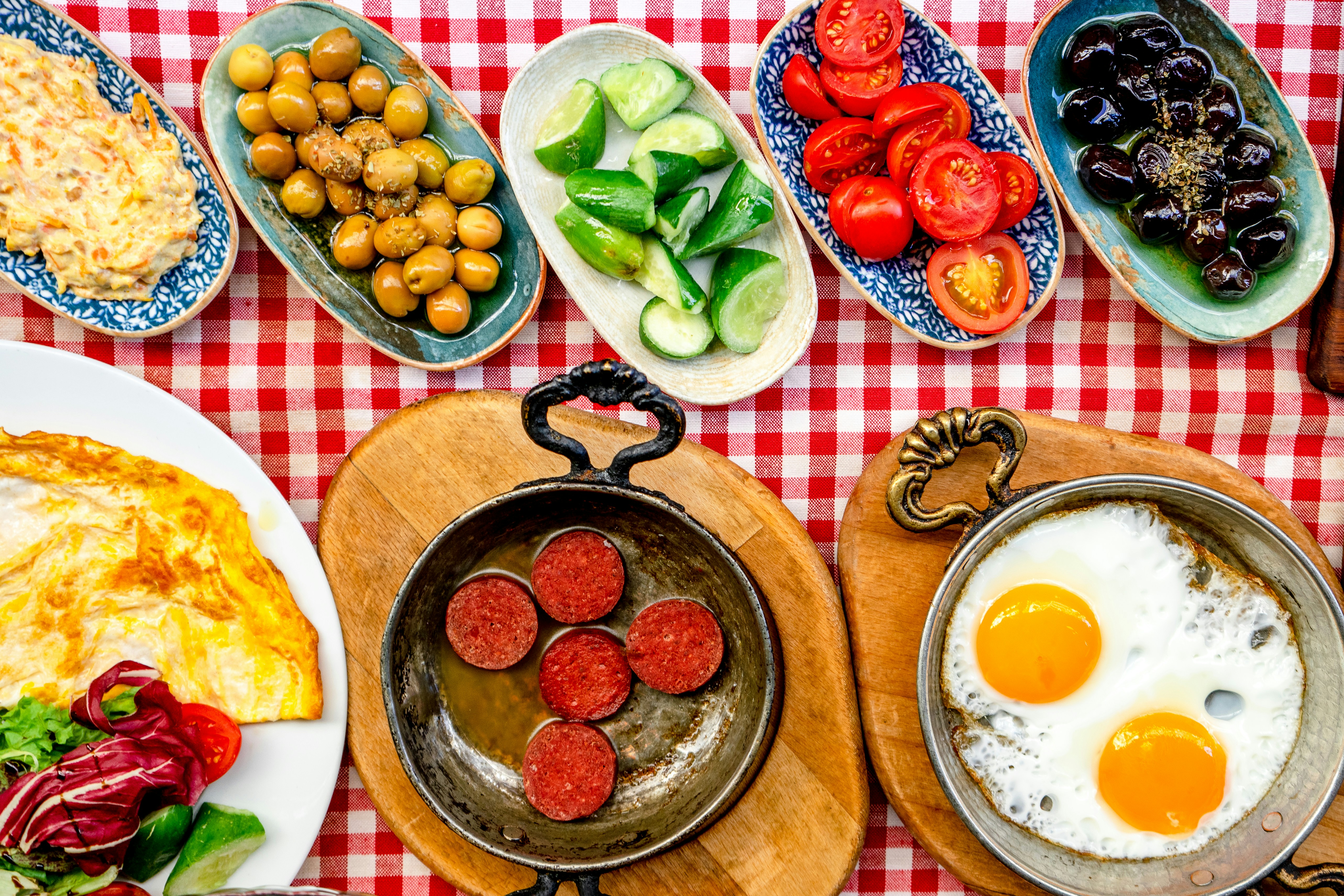 Turkish breakfast spread with eggs, sucuk sausage, olives, tomatoes and cheese on a red-checked tablecloth in Istanbul
