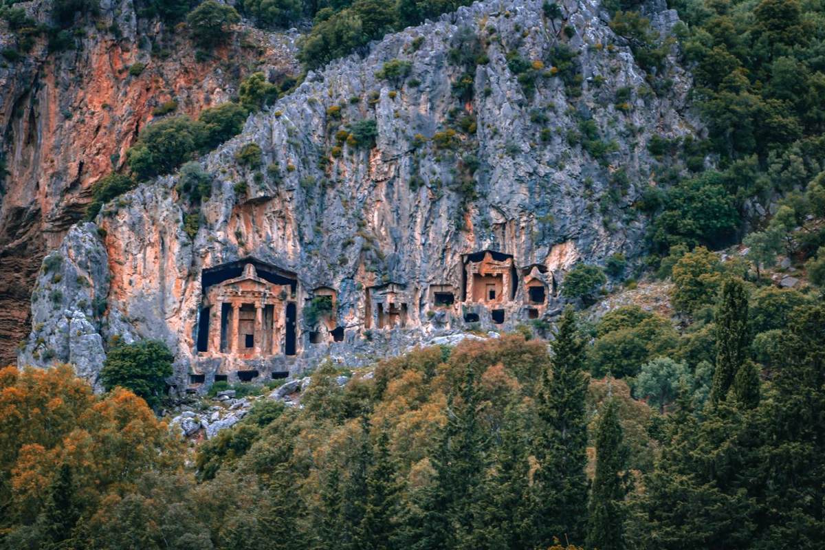 Lycian rock tombs carved into cliffs above forest