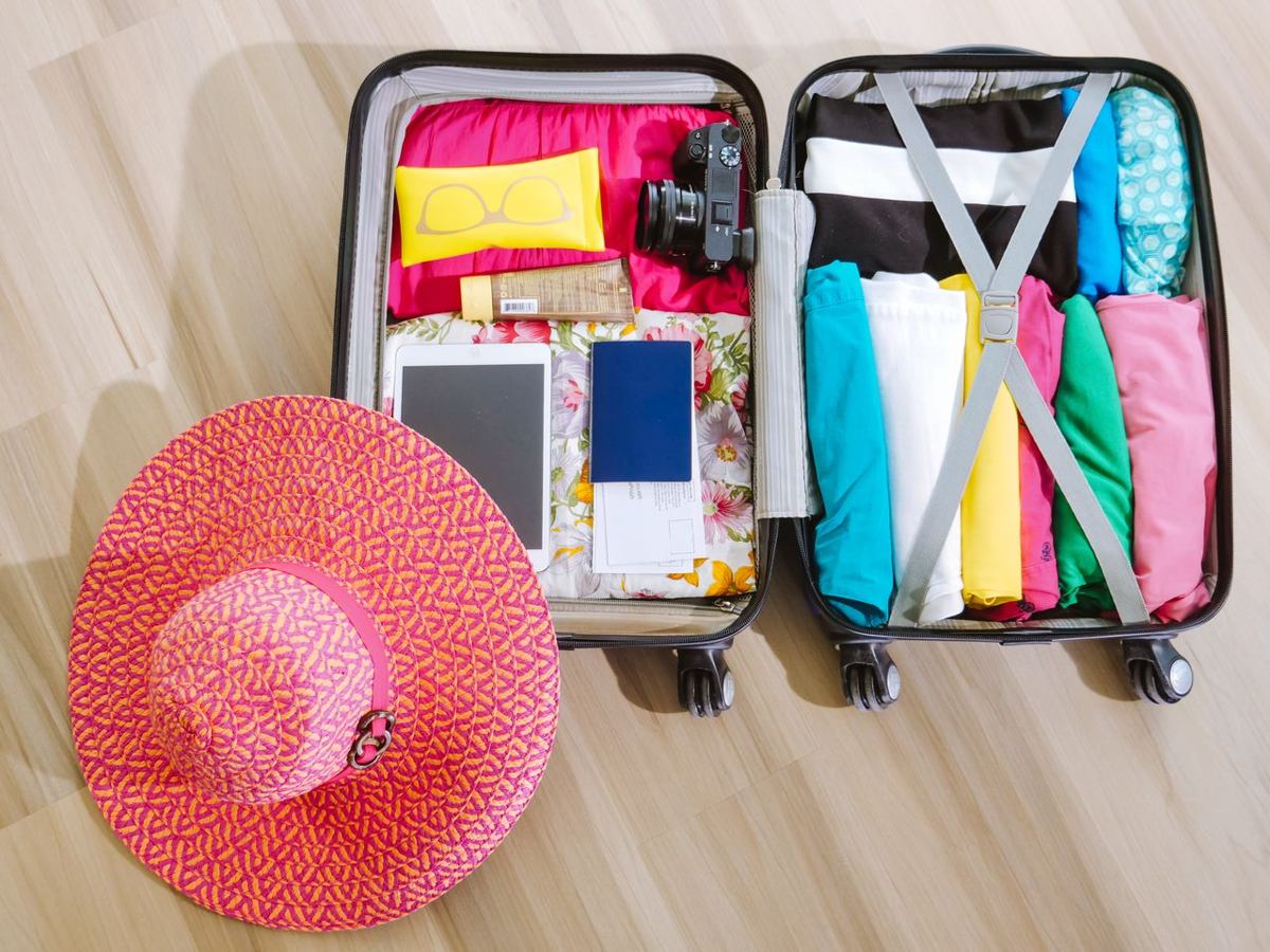 Top-down view of a suitcase packed with clothes, a camera and a sun hat