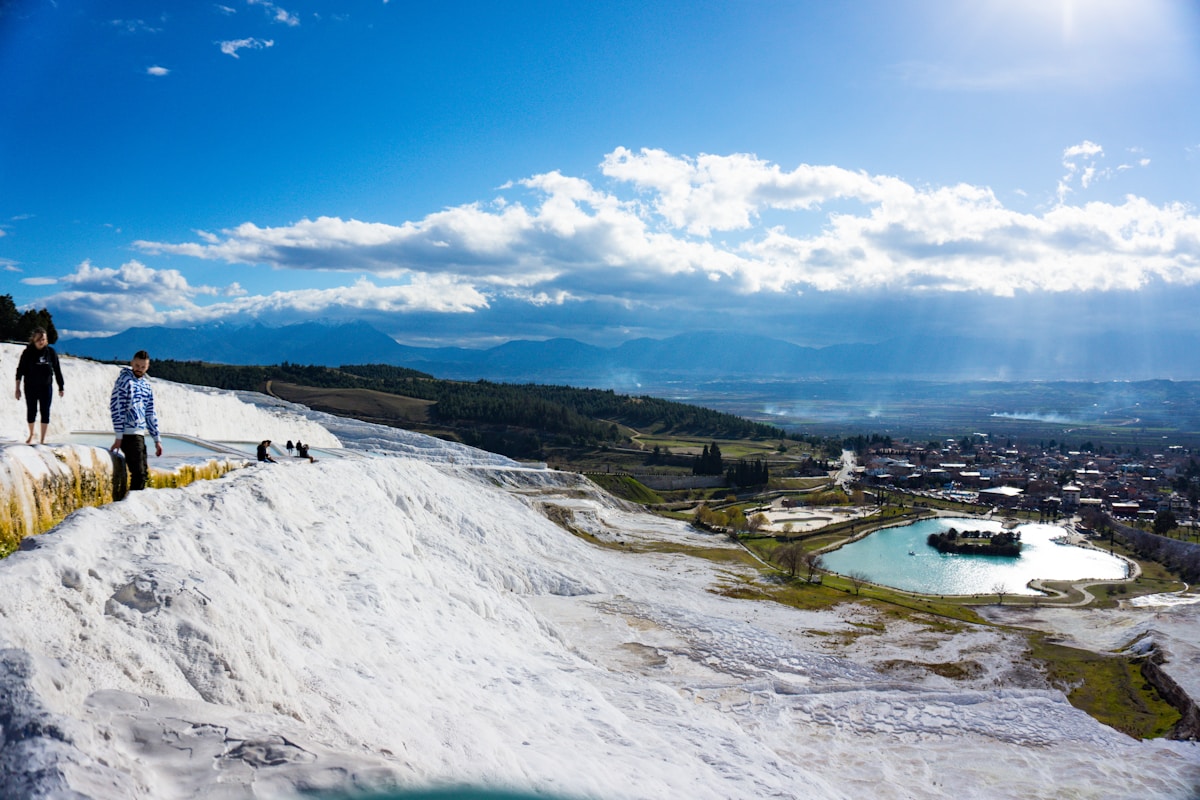 People walking on white travertine terraces overlooking Pamukkale village and thermal pool, Denizli, Turkey