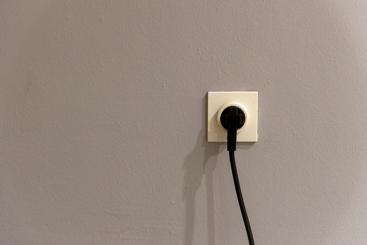 Cream European wall socket with a black two-pin plug on a grey wall