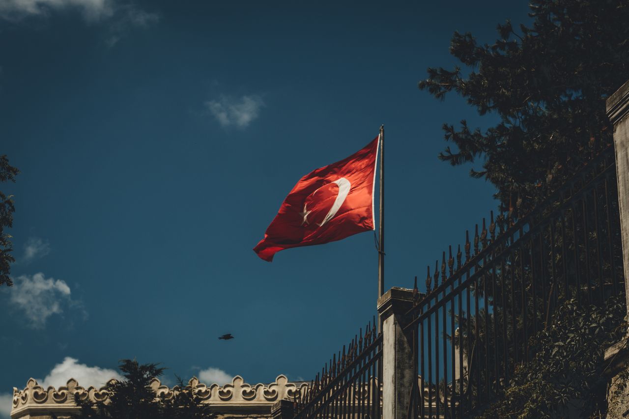 Turkish flag flying against a deep blue sky above an ornate stone wall in Istanbul