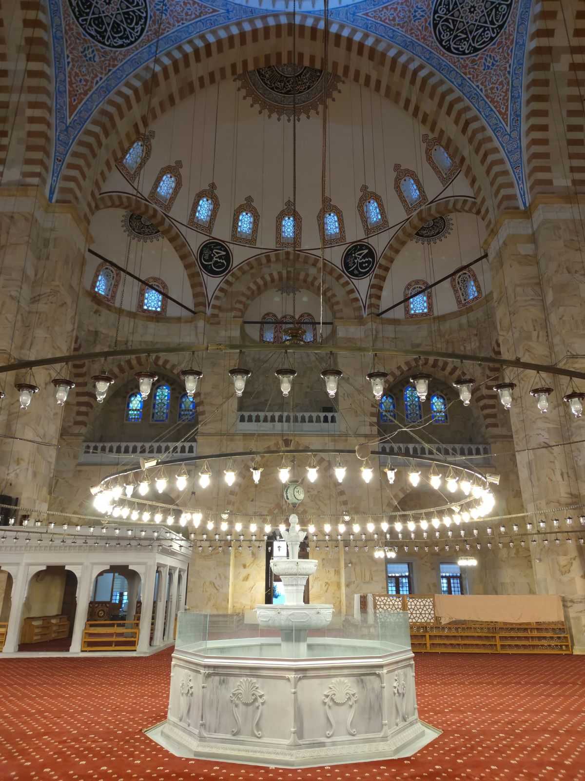 Interior of a Turkish mosque in Samsun showing the ornate dome, chandelier, and marble ablution fountain