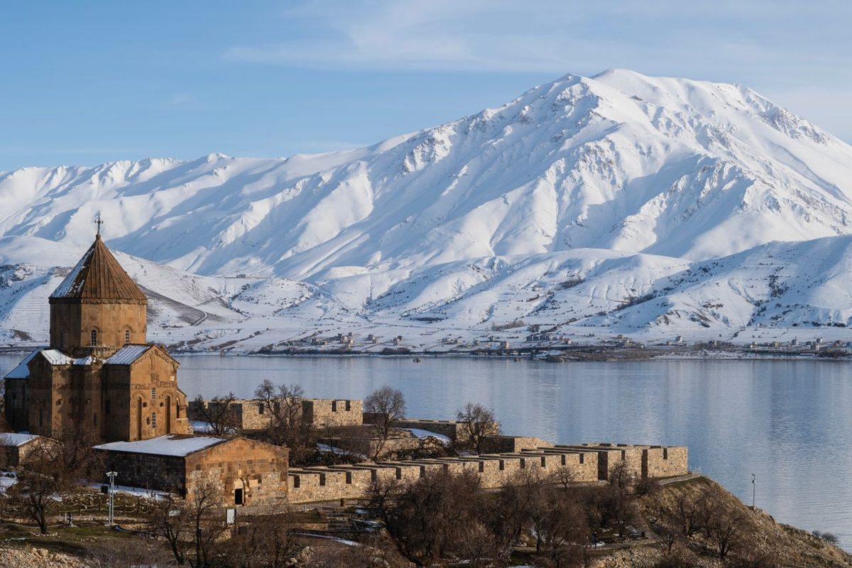Historic church by a calm lake with snowcapped mountains near Van